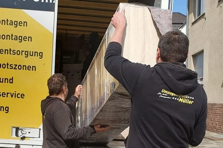 zwei umzugshelfer laden verpacktes moebelstueck in umzugswagen